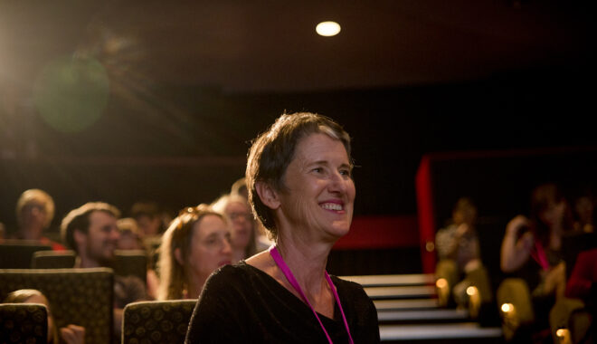 Sue Giles at a 2017 Polyglot Theatre 5678 Film Club event. She is seated in a cinema, looking at someone out of frame, smiling. Other people are visible behind her. Photographer: Theresa Harrison