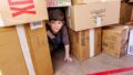 A We Built This City production photo. A child with short dark hair peers out from a tunnel made of cardboard boxes.