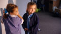 A Shadow Tricks workshop photo. Two students standing next to a tall screen look over their shoulders, their faces illuminated with light from a projector out of frame.