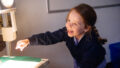 A Shadow Tricks workshop photo. A smiling student reaches towards an illuminated projector.