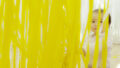 A Bellbird production photo. A baby sits behind hundreds of strands of suspended yellow and white ribbons.