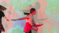 A Sound Shadows production photo. A child with a ponytail plays in front of a screen with red, green and blue coloured images on it. The child has one arm outstretched behind her and the other one in front of her. Photographer: Theresa Harrison