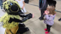 A Bees production photo. A performer in a bee costume outstretches their arms towards a child. The child covers their mouth in excitement. Photo: Libby Koba.