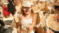 A Paper Planet production photo. A child wearing a handmade cardboard and paper costume smiles at the camera. The cardboard forest and other people are visible in the background.