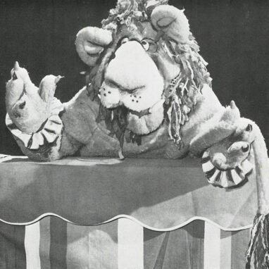 An image of 'Circus Star' by Dorothy Rickards. A puppet with a large nose and frilled sleeves poses on a striped counter.
