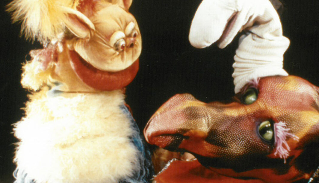 An 'Oddsocks and Snores' production photo. Three puppets are pictured against a black background. The puppet on the left is small and fluffy, and is smiling. There is a worm puppet and a dragon's head puppet.