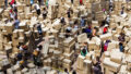 An aerial We Built This City production photo. Thousands of cardboard boxes fill a large space. People are scattered amongst them, building structures.
