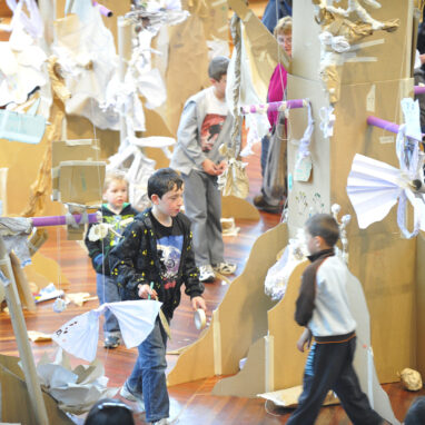 A Paper Planet Production photo. A child walks amongst cardboard trees decorated with steamers and paper and tape. Photo: Martin Reddy.