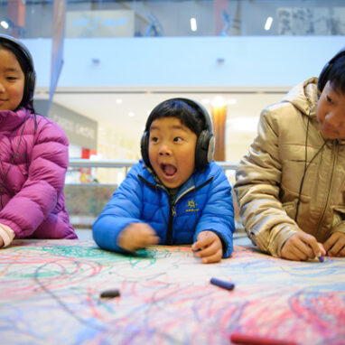 Three kids drawing with headphones on