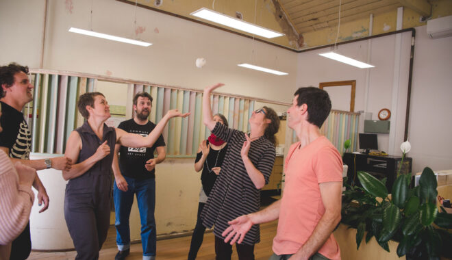 A professional development workshop photo. A group of artists play a game with a ball of scrunched masking tape, batting it to each other with their hands.