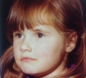 A child with brown eyes and shoulder length brown hair looks forward.