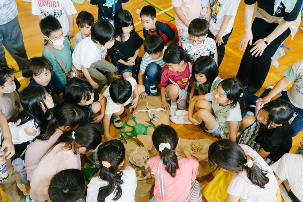 Paper Planet production photo: Ai Ueda. Children circle and kneel around multicoloured sea creatures created from papier-mache.