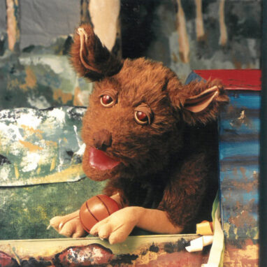 A 'Digger's Rest' production photo. A brown dog puppet holds a basketball.