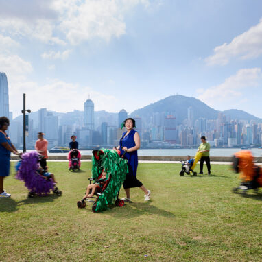 A Pram People (Hong Kong Edition) promo photo. Adults wearing headphones push prams decorated with brightly coloured ribbons on the Harbourside Lawn. Photo courtesy of Learning and Participation Team, Performing Arts Division, West Kowloon Cultural District