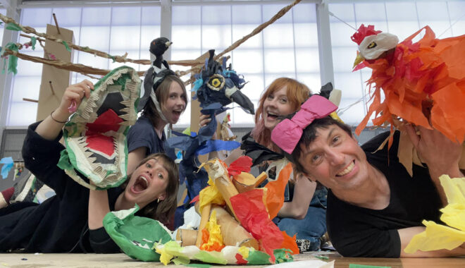 A behind-the-scenes photo of the creative team, Paper Planet in specialist schools. They smile at the camera, and hold up colourful paper creatures and creations. Photo: Nick Barlow.