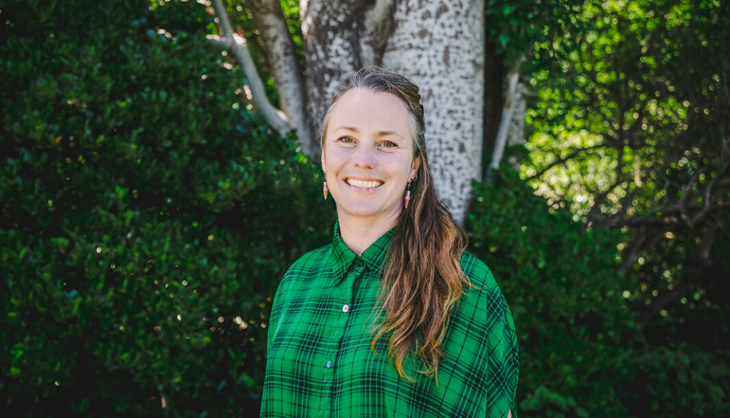 Polyglot co-CEO Cat smiles while standing in front of a tree. Cat wears a green collared shirt. Her long hair is draped over her left shoulder. Photo: Theresa Harrison