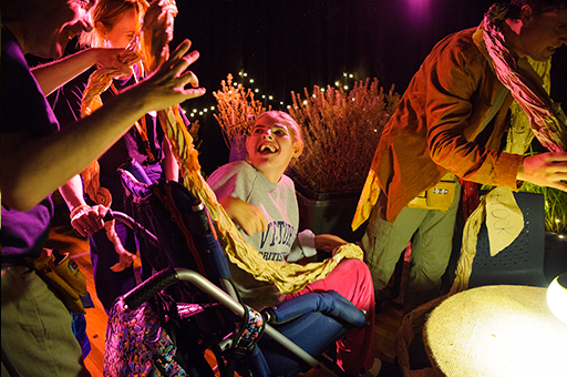 A child in a wheelchair smiles and looks back at Polyglot artists.