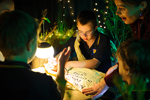 A child with glasses reads from a parchment paper.