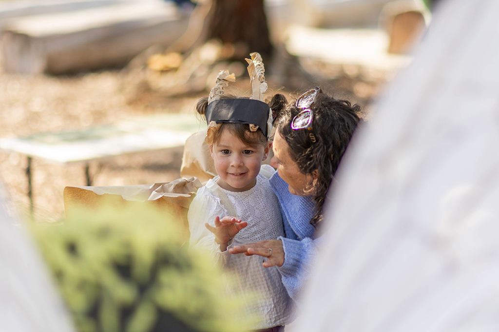 A Bees production photo. A small child in handmade paper wings and antennae and their adult engage with a Polyglot artist in an intricate black and yellow Bee costume. Photo: Royal Botanic Gardens Victoria.