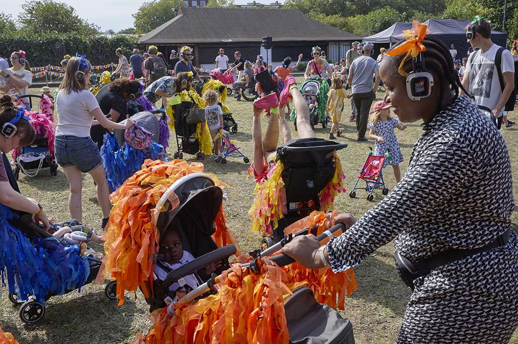 A Pram People production photo. Parents and carers wearing headphones push their children in prams, which are decorated with brightly coloured ribbons. Photo: David Levene, GDIF