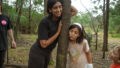 Forest production photo: Claudia Sangiorgi Dalimore. A Polyglot artist and a child lean on either side of a tree, smiling. Another child looks on.
