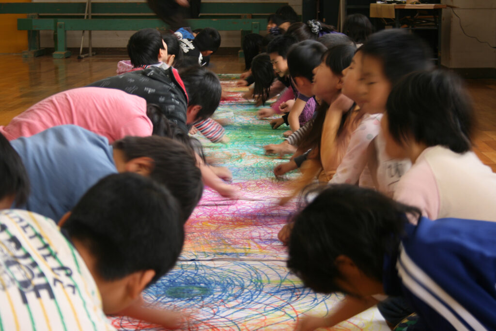 We Built This Town production photo: John Bailey. Children sit on the floor on either side of a long piece of paper, creating a large, colourful, shared abstract drawing.