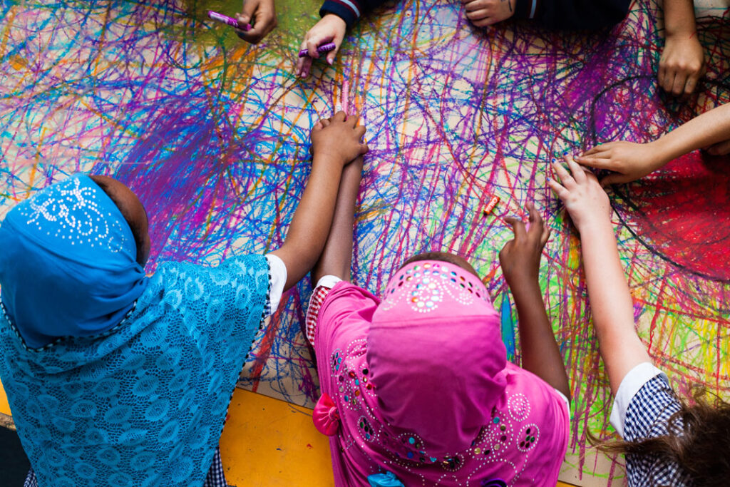 Sound of Drawing production photo: Kade Greenland. An overhead view of children, two of whom wear colourful headscarves, creating a large shared abstract drawing.