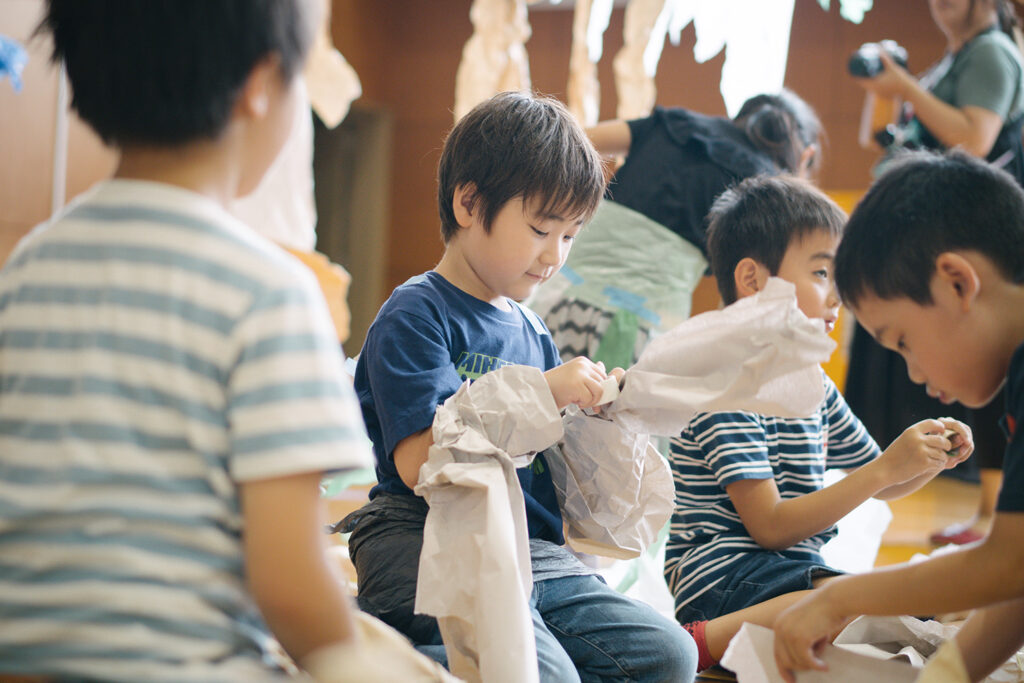 Paper Planet production photo: Ai Ueda. Children sit on the floor, creating and playing with paper and tape.