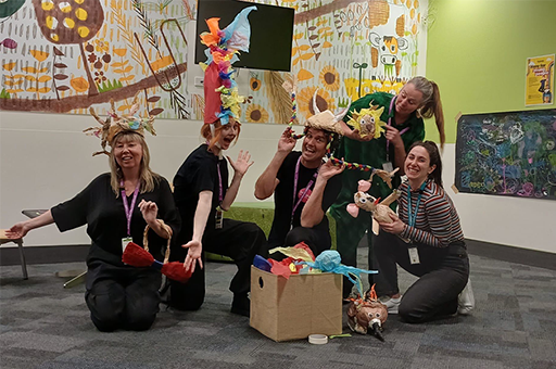 An Arts-Health session. Five adults wearing paper costumes pose in a waiting room. Photo: Cat Sewell