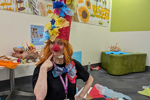 An Arts-Health session. A Polyglot artist wears a colourful paper costume and is seated on the floor of the waiting room. Photo: Cat Sewell
