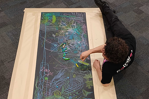 An Arts-Health session. A Polyglot artist draws with crayons on the floor. Photo: Cat Sewell