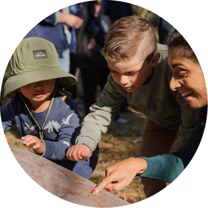 Forest production photo: Sarah Walker. Two children and a Polyglot artist closely inspect a tree trunk.