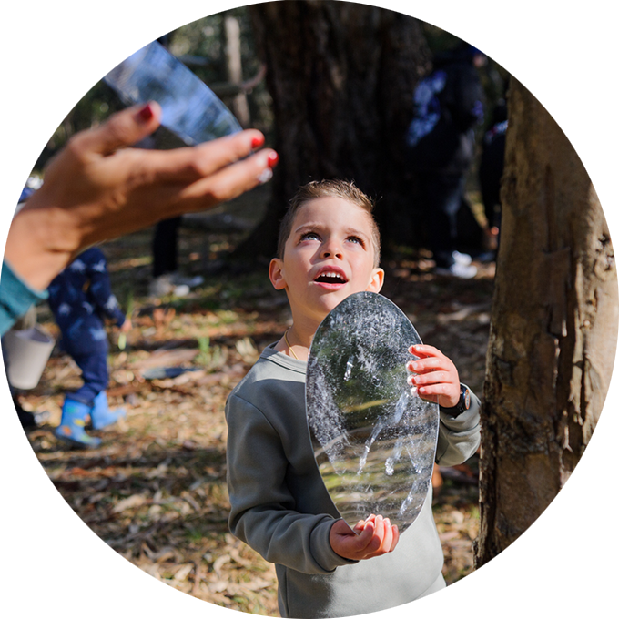 Forest production photo: Sarah Walker. A child holds a round mirror and gazes up to the sky.