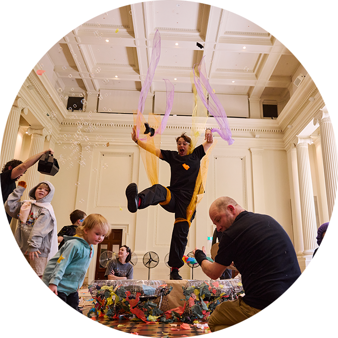 Whirlwind production photo: A Polyglot artist dances mid-motion, fabric flowing from her limbs as children and adults gather around her. Photo: Laura May Grogan.