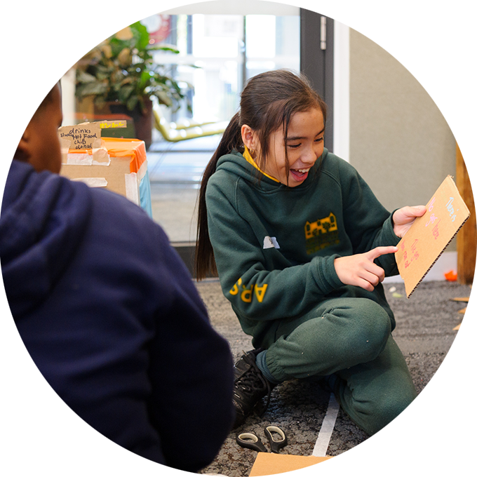 Wish Street production photo: A child laughs and gestures to a cardboard sign. Another child sits on the left-hand side. Photo: Sarah Walker.