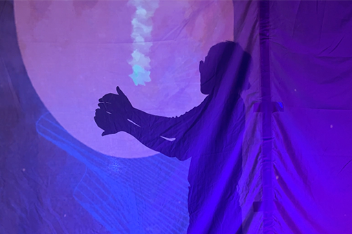 A silhouette of a Polyglot artist, against a a screen illuminated by a deep purple projection. They are holding out their hands to catch illustrated stars. Both images are in a darkened space.