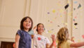 Whirlwind production photo: Laura May Grogan. Three children smile and play under a shower of colourful paper confetti.