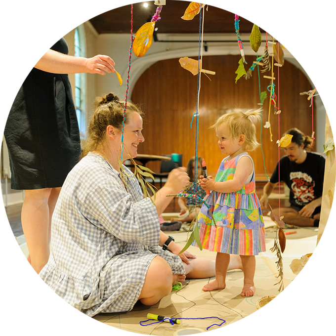Art Tree production photo: A parent and child play underneath the paper tree. There are other adults and children in the background. Photo: Sarah Walker.