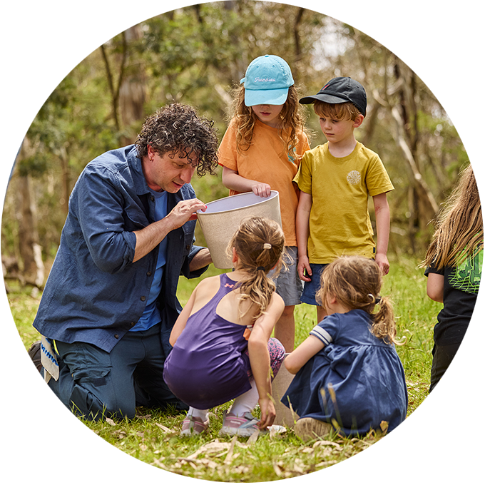 Forest production photo: Laura May Grogan. A Polyglot artist creates and plays with a group of children in a bushland clearing, using a cream-coloured lampshade.