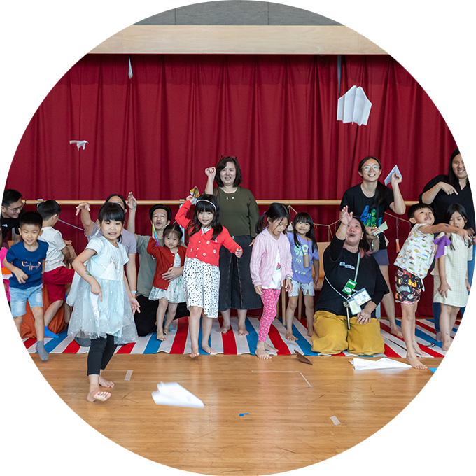 Pass it On: Children and their families throw paper planes into the air. They are grouped in a line. Photo: Alvin Ho