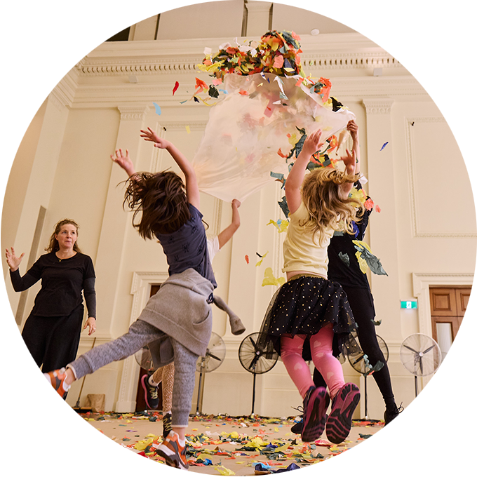 Whirlwind photo: Two children jump in the air as confetti falls from above. An AUSLAN interpreter and Polyglot artist are in the frame. Photo: Laura May Grogan.