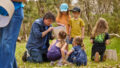 Forest production photo: Laura May Grogan. A Polyglot artist creates and plays with a group of children in a bushland clearing, using a cream-coloured lampshade.
