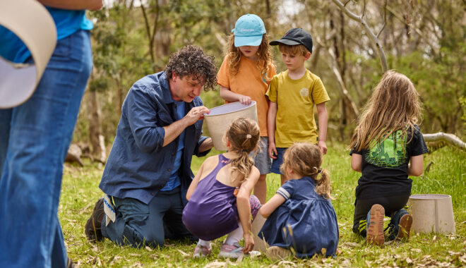 Forest production photo: Laura May Grogan. A Polyglot artist creates and plays with a group of children in a bushland clearing, using a cream-coloured lampshade.
