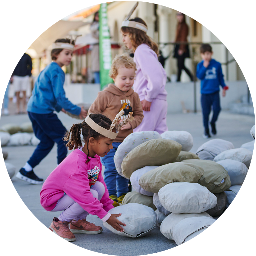 Ants production photo: Lucy Parakhina, Bondi Festival. Children wearing handmade paper antennae create a large formation from giant crumbs. They are outdoors on a paved surface.