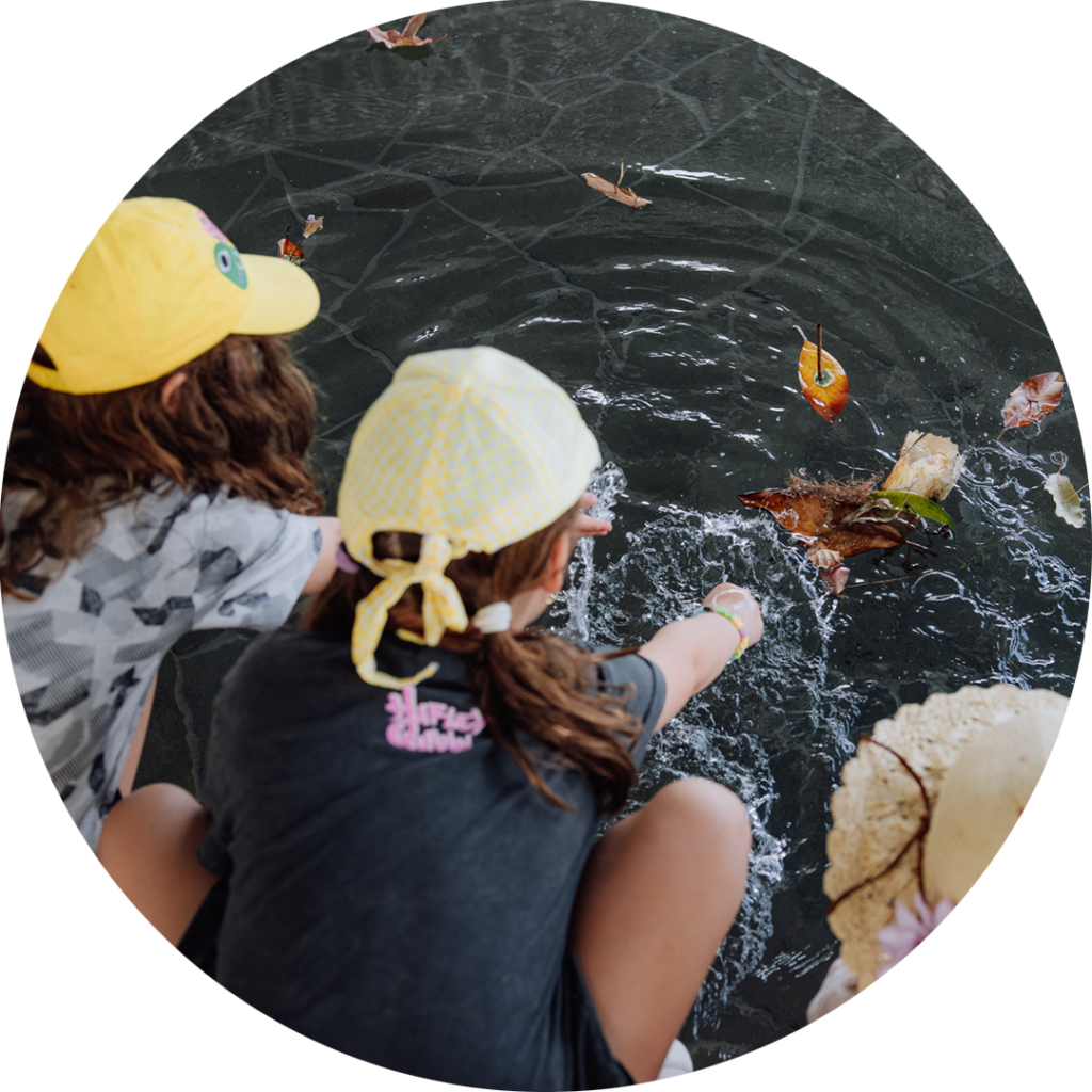 FLOAT production photo: William Hamilton-Coates, MPavilion. An overhead shot of three children leaning out over a reflecting pool, sailing small handmade boats made of leaves and twigs. The water ripples around their creations.