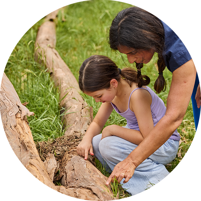 Forest production photo: Laura May Grogan. A child and Polyglot artist closely explore a tree trunk lying in green grass.