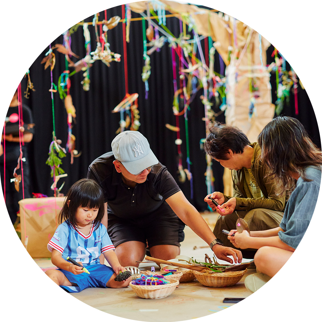 Art Tree production photo: Instant Crush, Moomba Festival. A family of four create and play under a wooden tree wrapped in brown paper. Creations hang from the tree with colourful yarn.