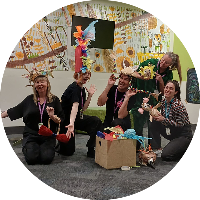 Polyglot Theatre and Centre for Community Child Health personnel pose for the camera, wearing or holding handmade paper creations.