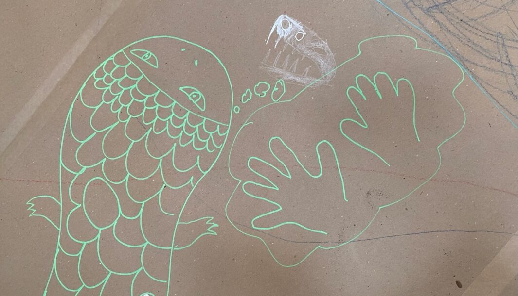Art Tree photo: Meg Taranto. A child's drawing in pale green paint pen of a fish and two hands on brown cardboard.