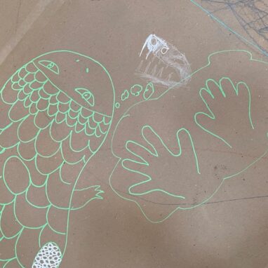 Art Tree photo: Meg Taranto. A child's drawing in pale green paint pen of a fish and two hands on brown cardboard.